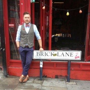 Dapper Chap standing by Brick Lane street sign