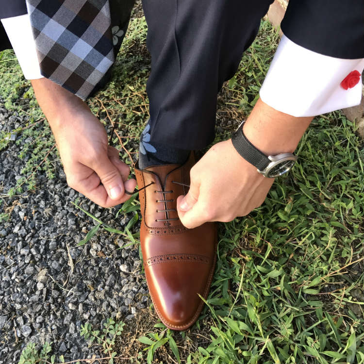 man in french cuffs tying brown shoes