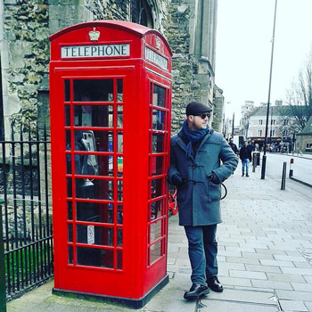 Man In Duffel Coat & Flat Cap Leaning On Red Phonebox
