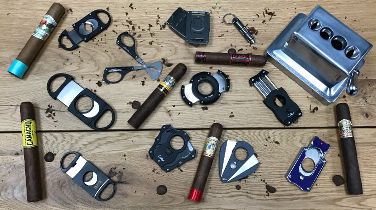 Different Cigar Cutters With Cigars On Wooden Table